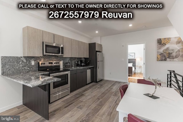 kitchen featuring light stone counters, backsplash, hardwood / wood-style flooring, stainless steel appliances, and a breakfast bar area