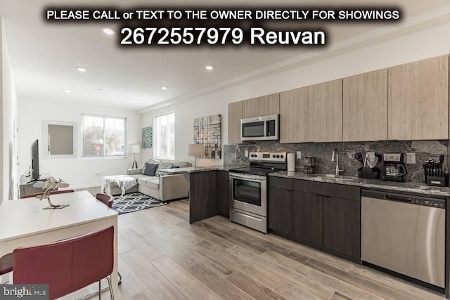 kitchen with decorative backsplash, light hardwood / wood-style floors, stainless steel appliances, dark stone counters, and sink