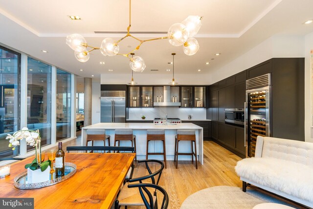 kitchen featuring high end appliances, tasteful backsplash, gray cabinetry, wall chimney exhaust hood, and light wood-type flooring