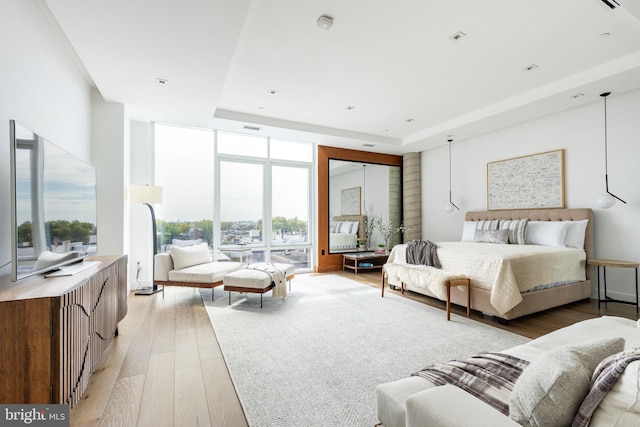 bedroom featuring light hardwood / wood-style flooring, multiple windows, a raised ceiling, and expansive windows