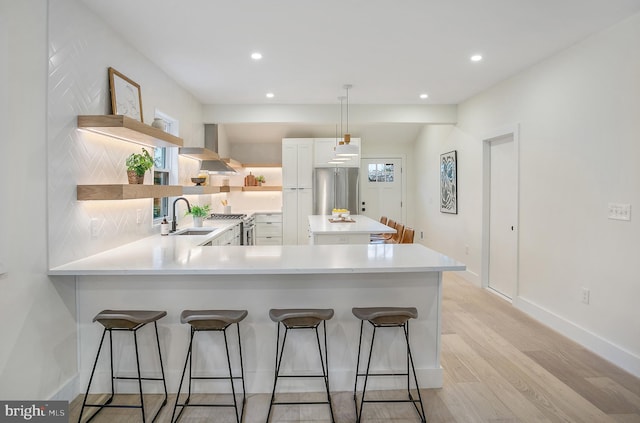 kitchen with wall chimney range hood, kitchen peninsula, sink, premium appliances, and white cabinetry