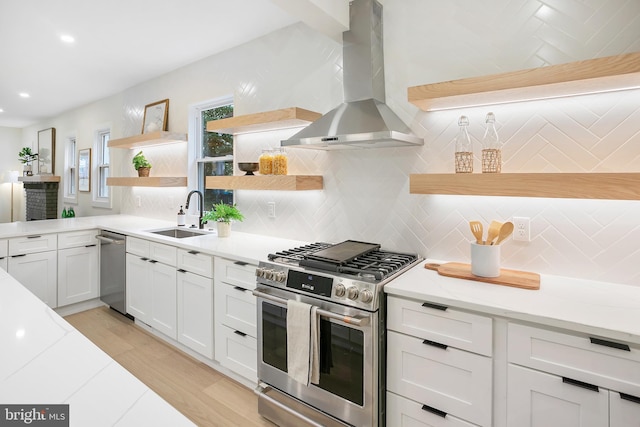 kitchen with sink, stainless steel appliances, wall chimney range hood, tasteful backsplash, and white cabinets