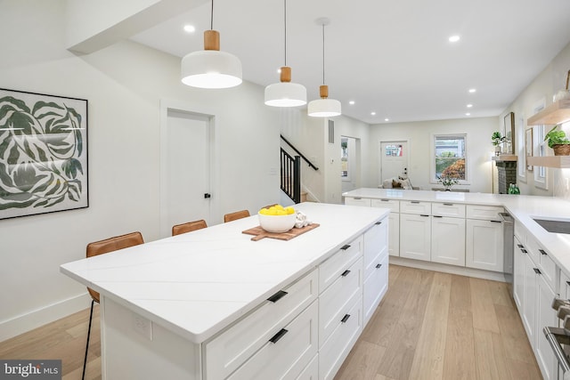 kitchen featuring a center island, hanging light fixtures, light hardwood / wood-style floors, a kitchen bar, and kitchen peninsula