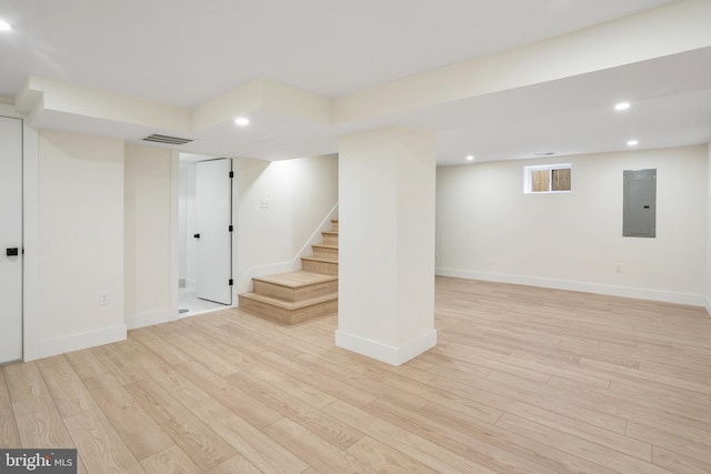 basement featuring electric panel and light hardwood / wood-style flooring