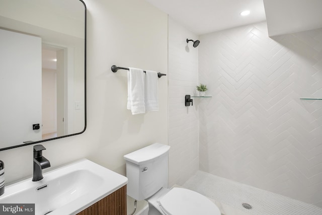 bathroom featuring a tile shower, vanity, and toilet