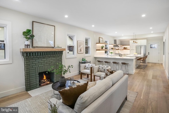 living room featuring light wood-type flooring, sink, and a brick fireplace