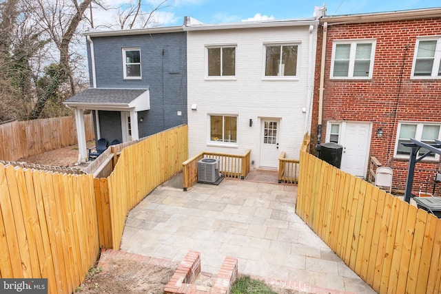 rear view of house featuring a patio, brick siding, central AC, and a fenced backyard