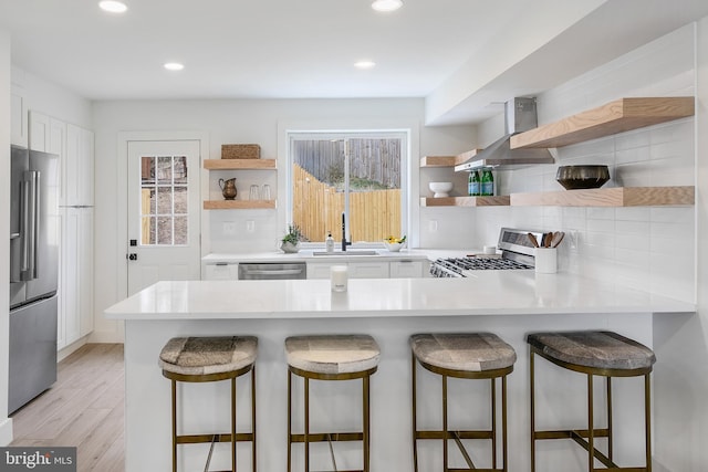 kitchen featuring open shelves, a sink, stainless steel appliances, white cabinetry, and wall chimney exhaust hood