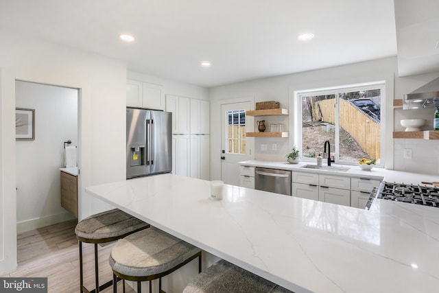 kitchen featuring light stone counters, a sink, appliances with stainless steel finishes, and open shelves