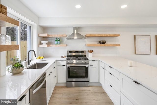 kitchen with open shelves, appliances with stainless steel finishes, a sink, and wall chimney range hood