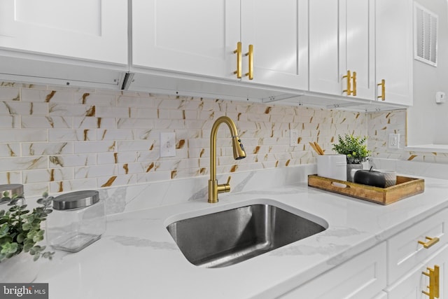 kitchen featuring white cabinets, light stone countertops, backsplash, and sink