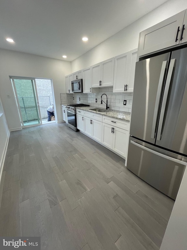 kitchen featuring appliances with stainless steel finishes, white cabinetry, light stone counters, light hardwood / wood-style flooring, and sink