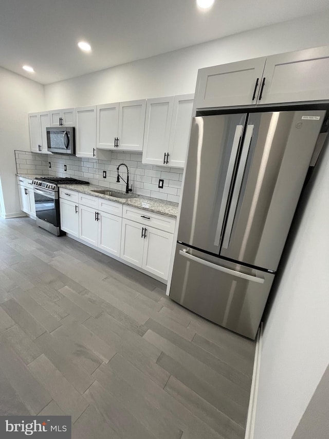 kitchen featuring white cabinets, sink, appliances with stainless steel finishes, light stone countertops, and decorative backsplash