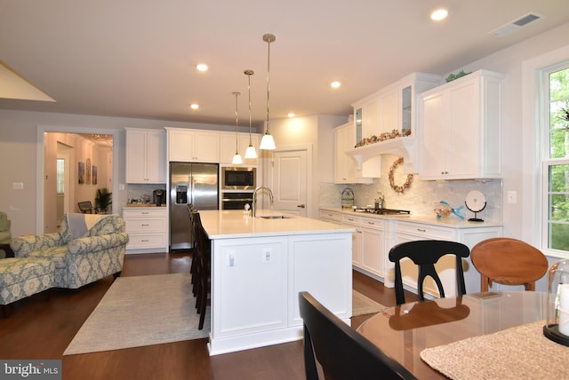 kitchen with appliances with stainless steel finishes, hanging light fixtures, decorative backsplash, white cabinets, and a kitchen island with sink