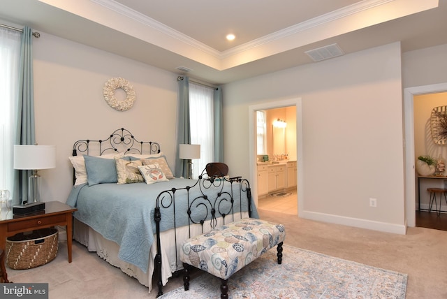 bedroom featuring light carpet, a tray ceiling, ensuite bathroom, and crown molding