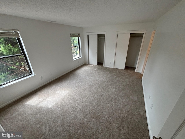 unfurnished bedroom featuring carpet floors, a textured ceiling, and multiple closets