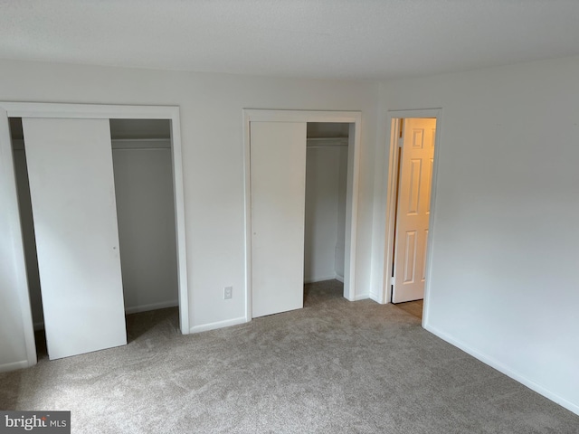 unfurnished bedroom with two closets and light colored carpet