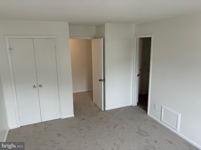 unfurnished bedroom featuring light carpet, a closet, and a textured ceiling