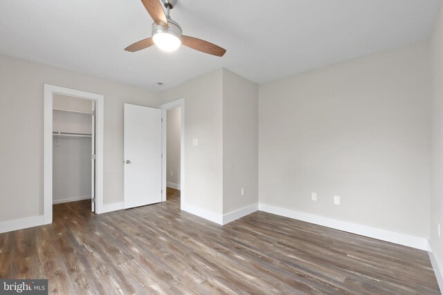 unfurnished bedroom featuring a spacious closet, ceiling fan, dark wood-type flooring, and a closet