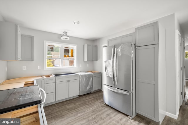 kitchen featuring gray cabinetry, light wood-type flooring, range, and stainless steel fridge