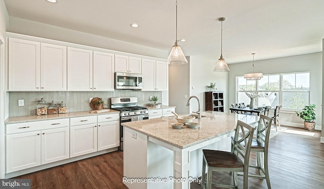 kitchen with dark wood-type flooring, white cabinets, pendant lighting, stainless steel appliances, and a kitchen island with sink