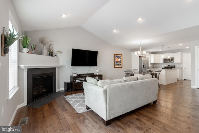 living room with a notable chandelier, vaulted ceiling, and dark hardwood / wood-style flooring