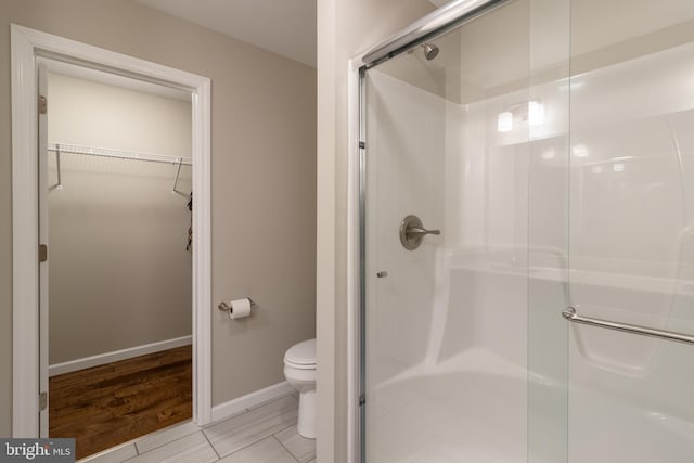 bathroom with hardwood / wood-style flooring, a shower with shower door, and toilet