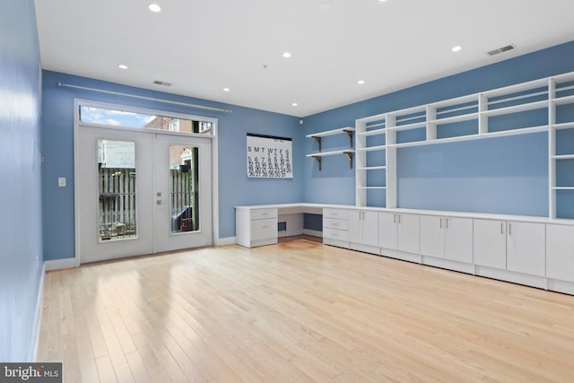 unfurnished living room featuring built in desk, light hardwood / wood-style floors, and french doors