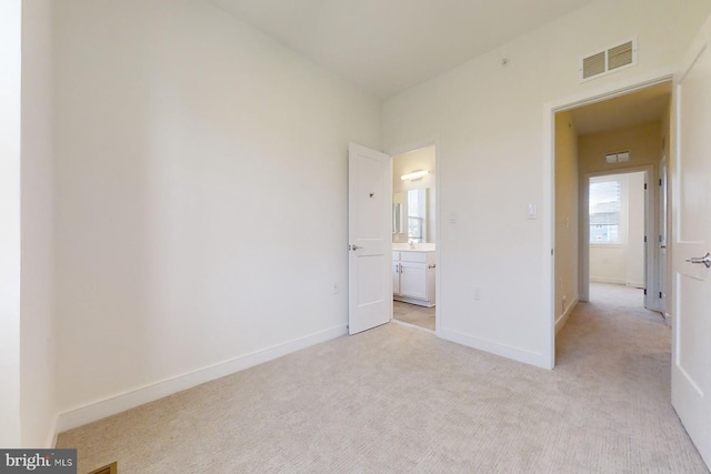 unfurnished bedroom featuring connected bathroom and light carpet