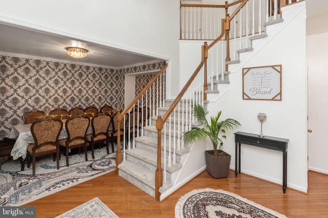 staircase with wood-type flooring, a chandelier, and ornamental molding