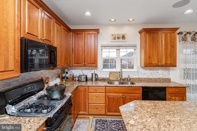 kitchen with decorative backsplash, black appliances, light stone counters, and sink