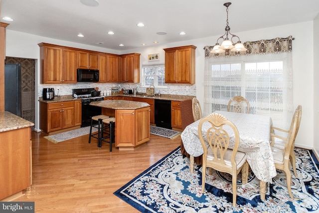 kitchen featuring light stone counters, a kitchen island, black appliances, light hardwood / wood-style flooring, and a notable chandelier