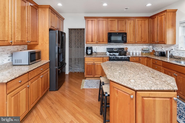 kitchen featuring black appliances, light hardwood / wood-style floors, a center island, and light stone counters