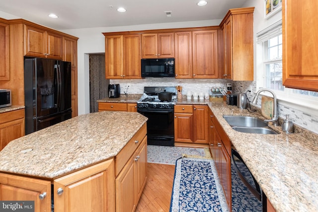 kitchen featuring light stone countertops, light wood-type flooring, black appliances, a center island, and sink