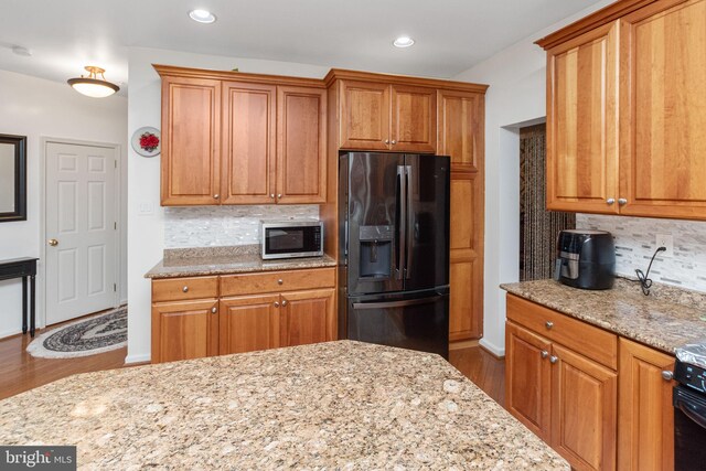 kitchen featuring fridge with ice dispenser, decorative backsplash, hardwood / wood-style floors, and light stone counters