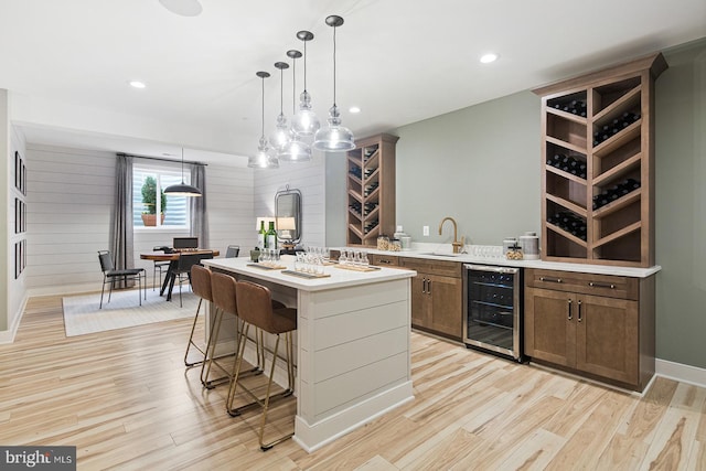 kitchen with light wood-style floors, a kitchen breakfast bar, a center island, light countertops, and wine cooler