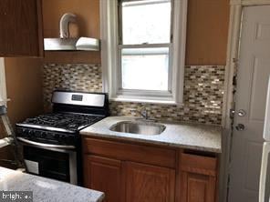 kitchen featuring a healthy amount of sunlight, decorative backsplash, stainless steel gas stove, and sink