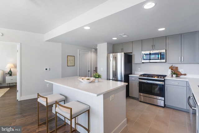 kitchen featuring appliances with stainless steel finishes, a breakfast bar, gray cabinets, light wood-type flooring, and a center island