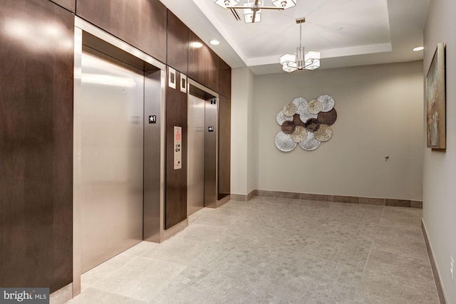 hallway featuring an inviting chandelier, a tray ceiling, and elevator