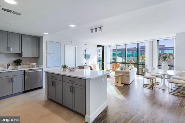 kitchen with sink, stainless steel dishwasher, light hardwood / wood-style flooring, gray cabinets, and a center island