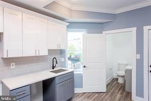 kitchen with ornamental molding, sink, backsplash, white cabinetry, and hardwood / wood-style flooring