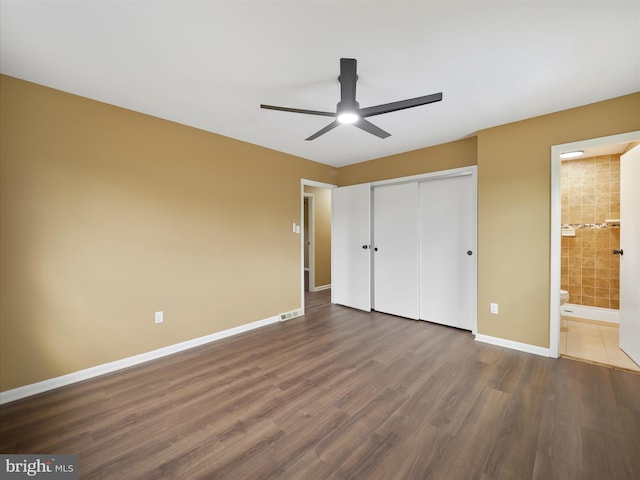 unfurnished bedroom with ceiling fan, a closet, connected bathroom, and dark hardwood / wood-style flooring