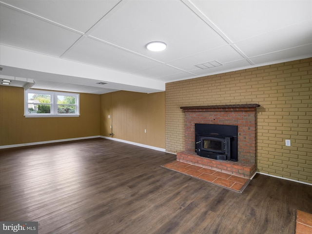 unfurnished living room with a wood stove, wood walls, a fireplace, dark hardwood / wood-style flooring, and brick wall