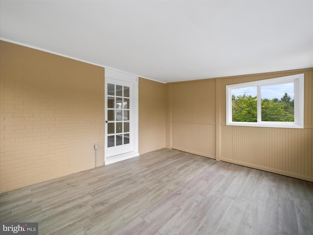 spare room featuring brick wall, wood walls, and light hardwood / wood-style floors