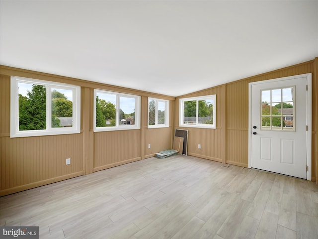 entrance foyer featuring light wood-type flooring, vaulted ceiling, wood walls, and plenty of natural light