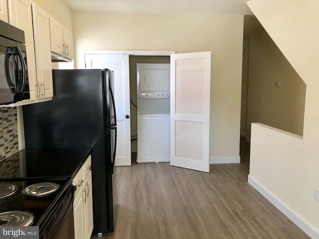 kitchen with black appliances, white cabinets, stacked washer and dryer, and light wood-type flooring