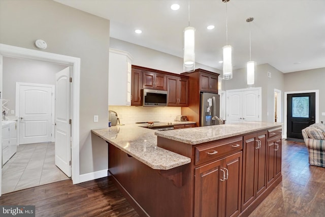 kitchen with pendant lighting, kitchen peninsula, tasteful backsplash, wood-type flooring, and stainless steel appliances