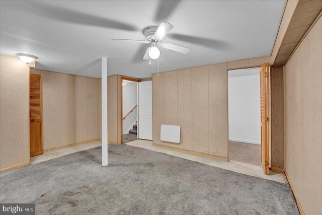 basement with ceiling fan, light colored carpet, and wood walls