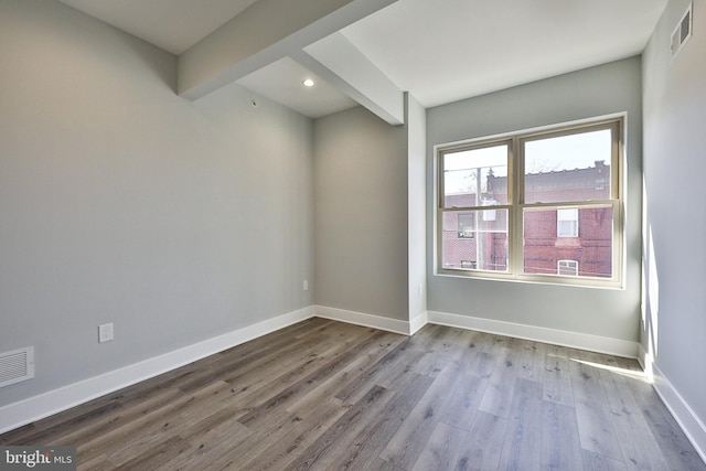 spare room featuring beam ceiling and light hardwood / wood-style flooring