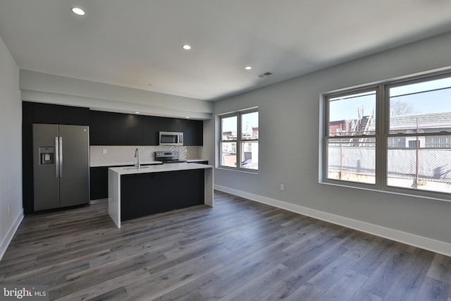 kitchen featuring appliances with stainless steel finishes, tasteful backsplash, a kitchen island with sink, dark hardwood / wood-style floors, and sink